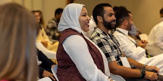 With a smile, a scarf-clad woman in the audience looks straight ahead.