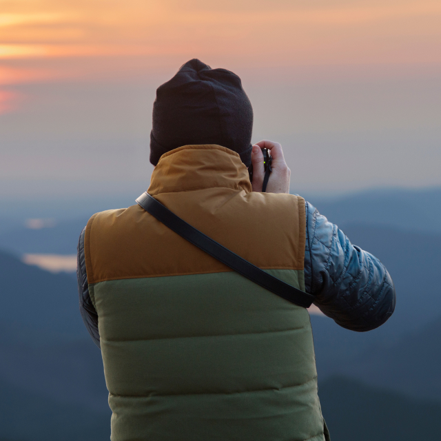 Looking over the shoulder of a person taking a photo of a mountain sunset.