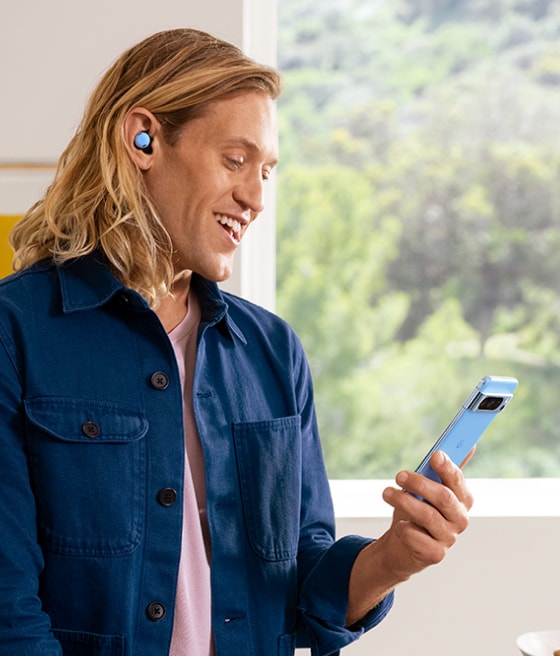 A person smiles at their Pixel 8 while using their Pixel Buds to talk on the phone.