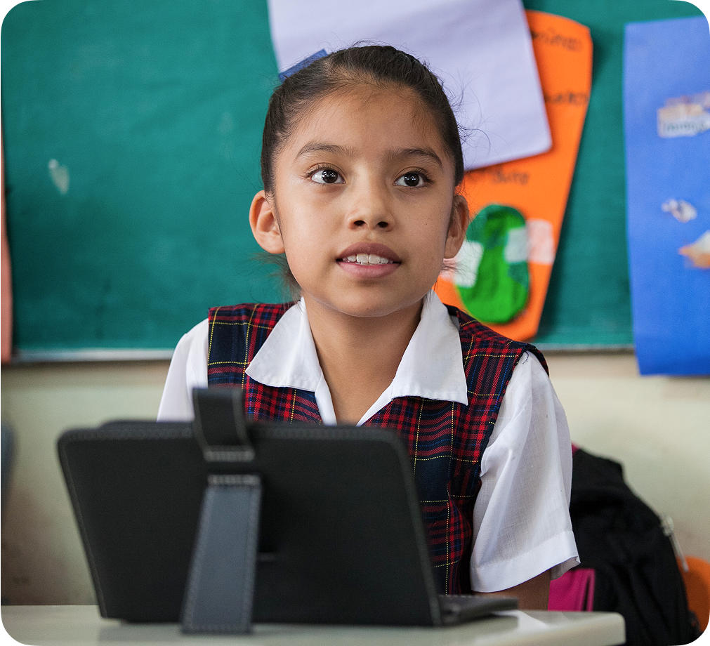 Un niño sonriente sentado en un escritorio de un aula frente a un dispositivo Chromebook.