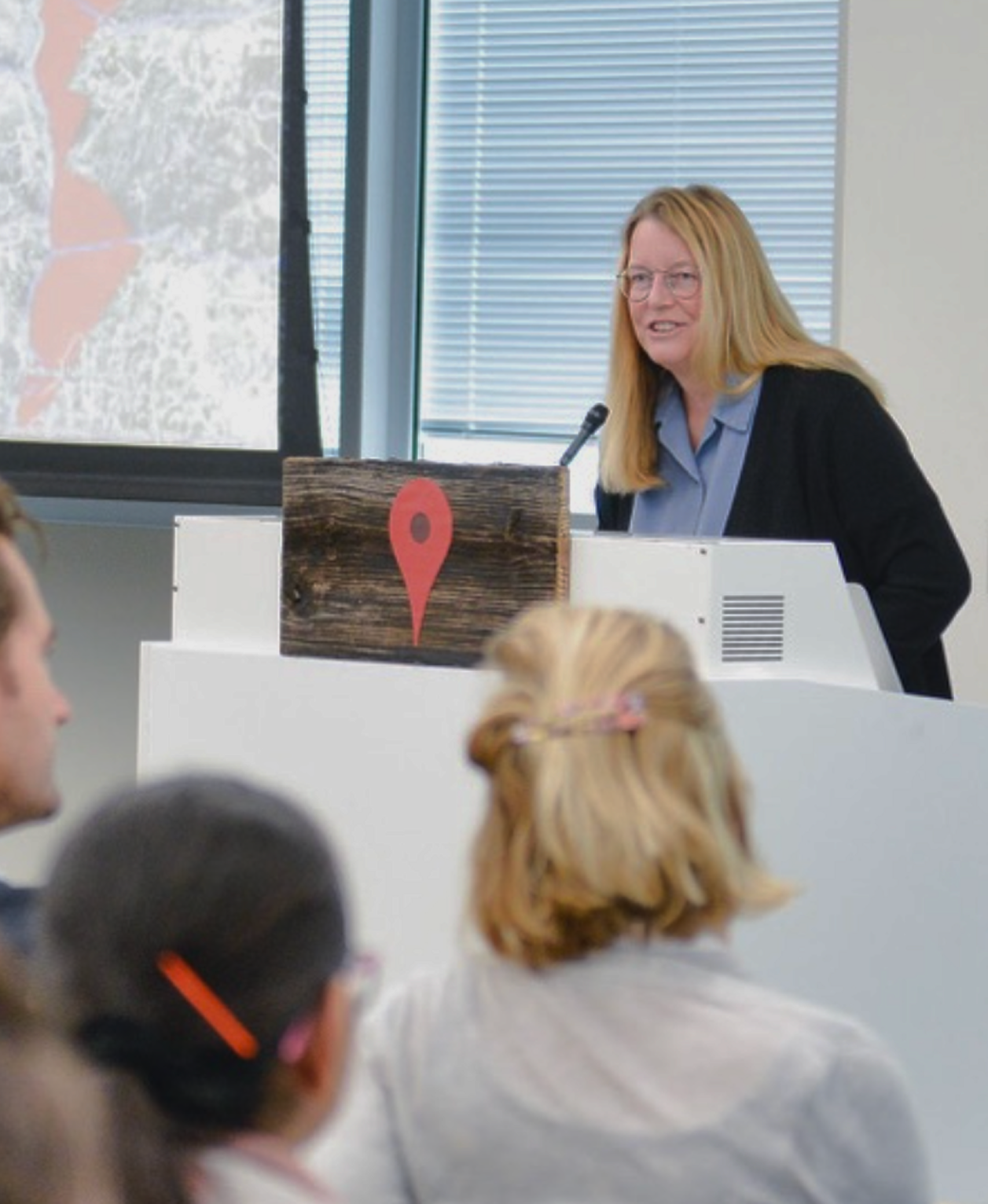 A woman giving a lecture with a geographic map behind her